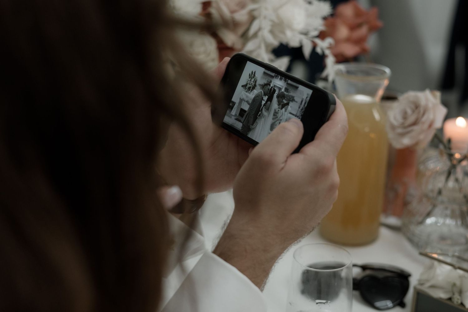 Someone holds a smartphone taking photos of floral arrangements on a table with beverage glasses.