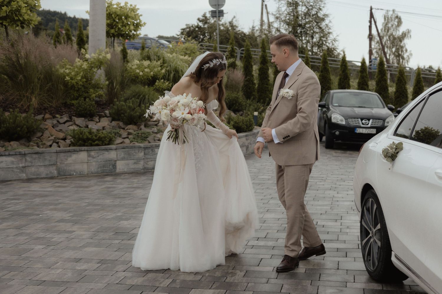 A couple in wedding attire stands together in a parking lot during a celebratory moment.