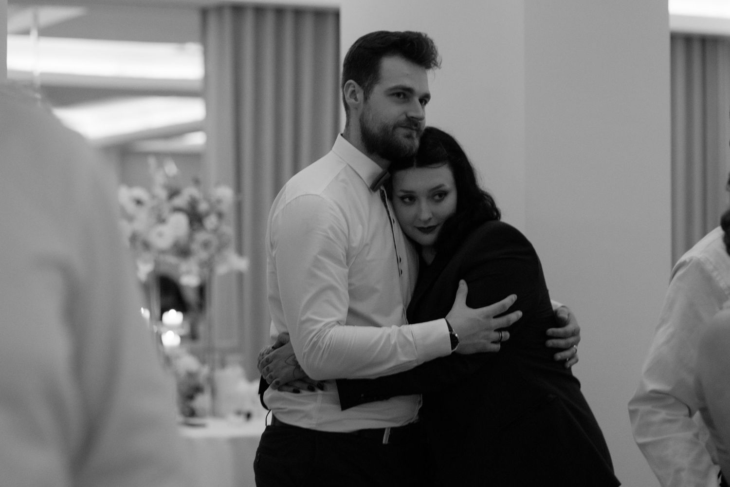 A couple slow dances together in an intimate embrace at a formal event, captured in black and white photography.