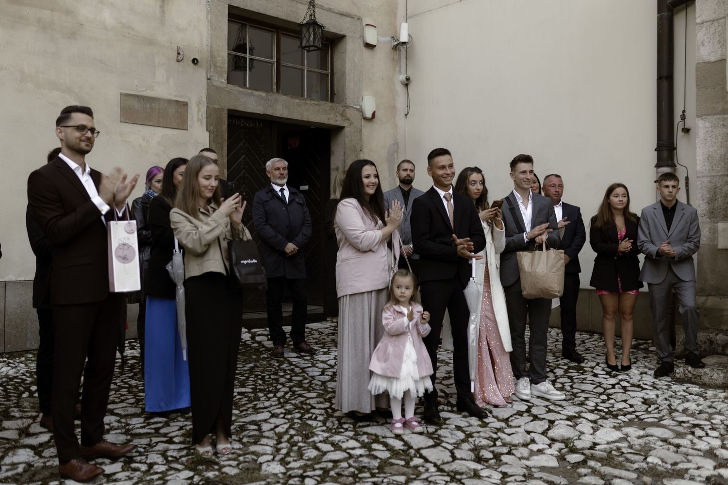 A group stands together for a formal gathering on a decorative stone floor in muted tones.