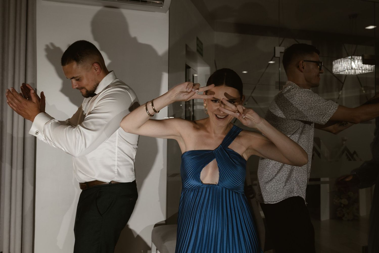 Guests dancing energetically while posing at a party, with one wearing a blue pleated dress and another in a white shirt.