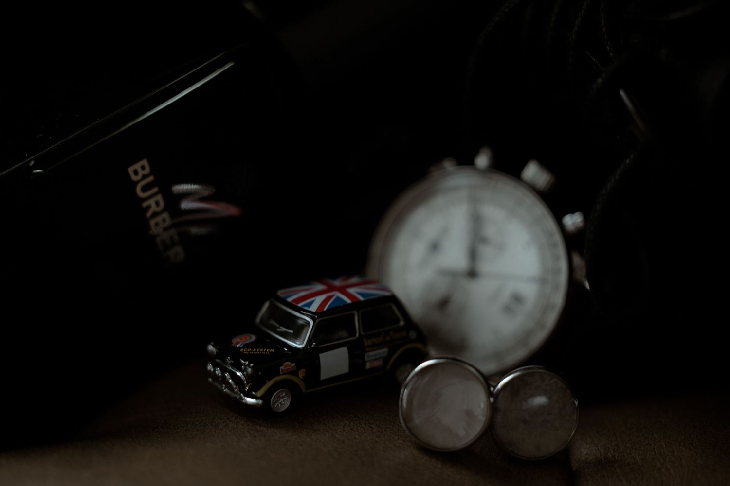 A vintage toy car sits alongside pocket watches in a moody, dark-toned still life composition.