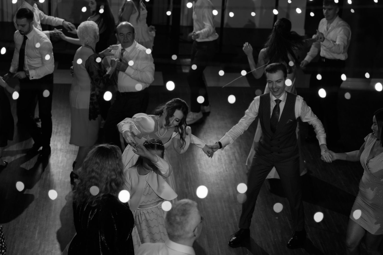 Dancing guests enjoy a lively reception under twinkling string lights on a dimly lit dance floor.