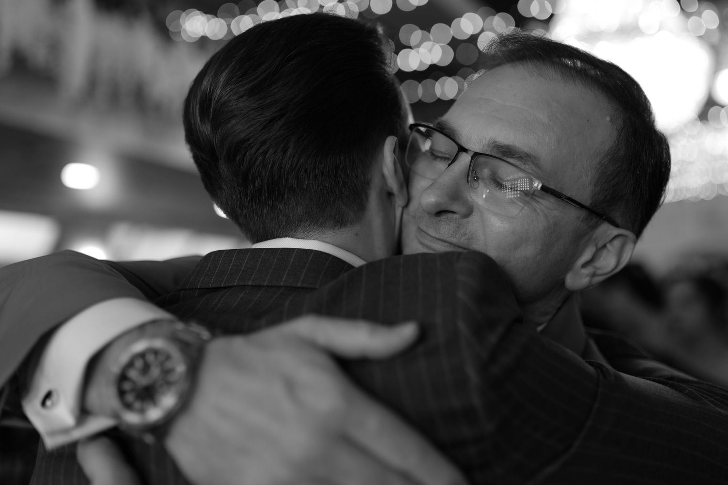 Two people embrace in formal attire at an event, captured in intimate black and white photography.