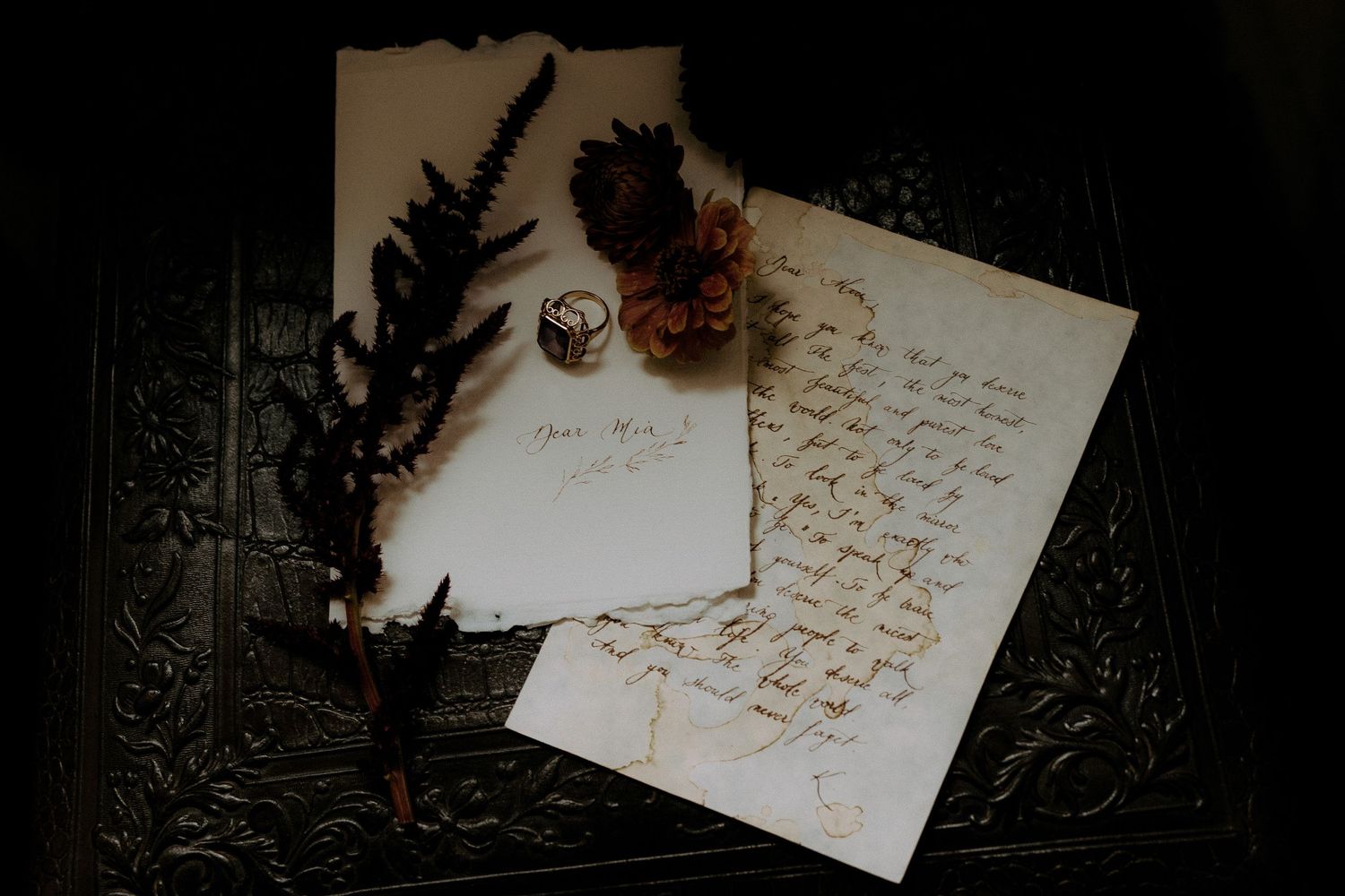 Vintage handwritten letter with feathers and worn parchment paper on dark textured background.