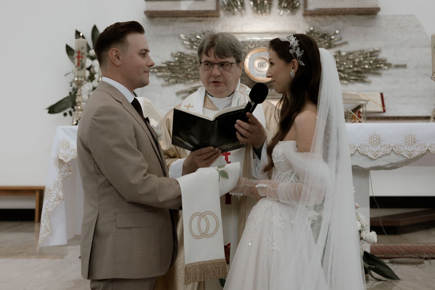 A wedding ceremony takes place in a church as the officiant reads from a book during the intimate service.