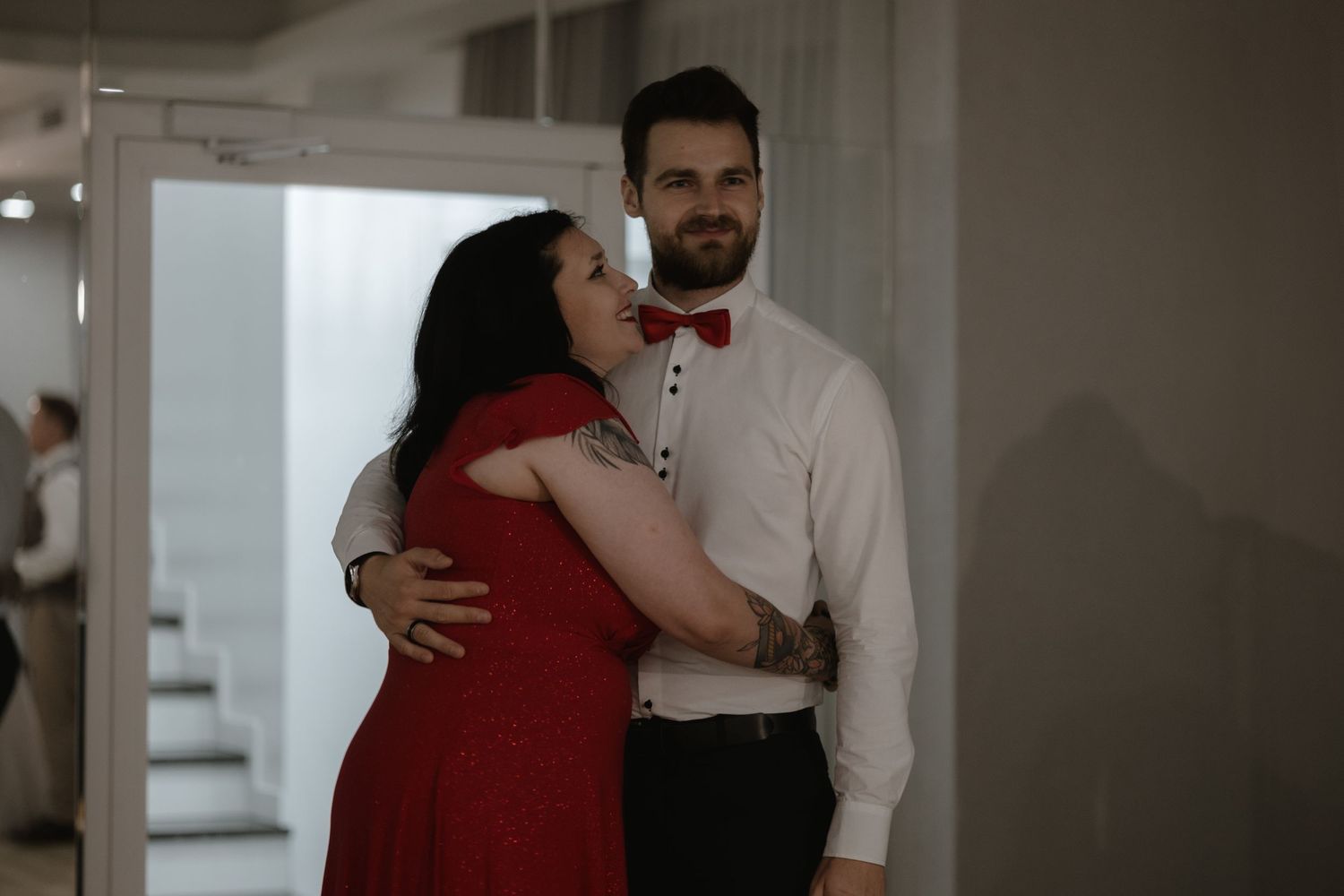 A couple dressed in red and white formal attire embrace while dancing at an indoor venue.