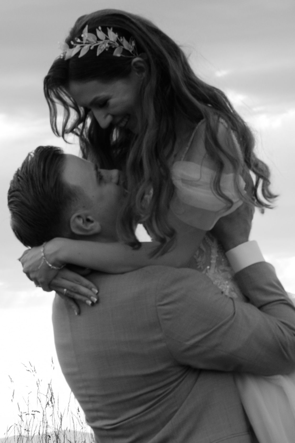 A romantic black and white wedding photo showing a couple embracing outdoors with the bride wearing a leaf crown headpiece.