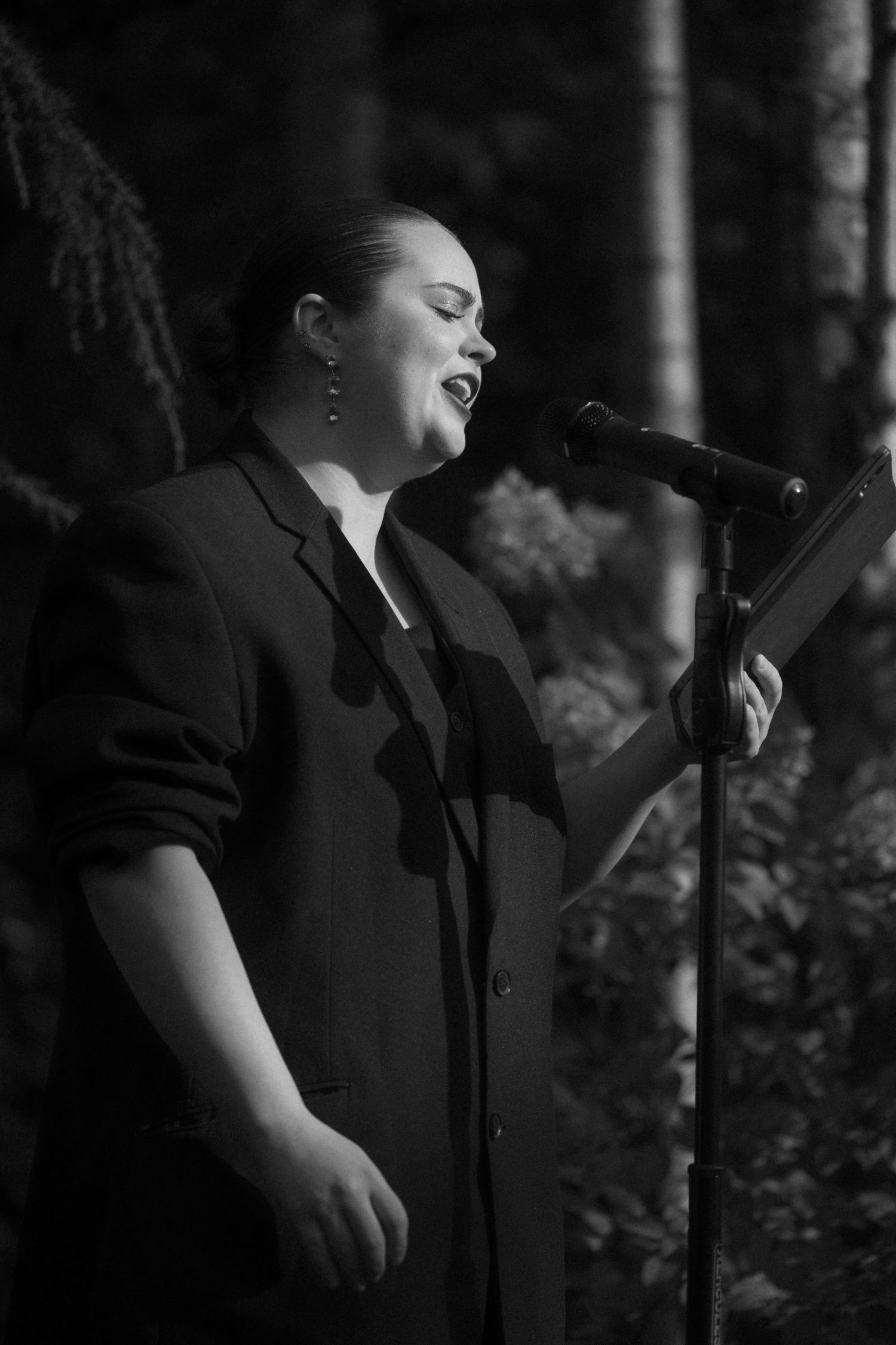 A singer in a black outfit performs passionately against a dark forest backdrop in a series of dramatic poses.