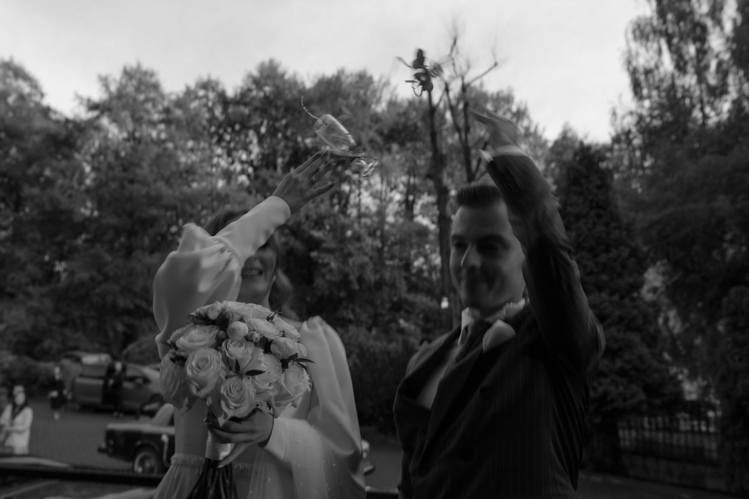 Two people in formal attire gesturing dramatically outdoors in a black and white vintage photograph.