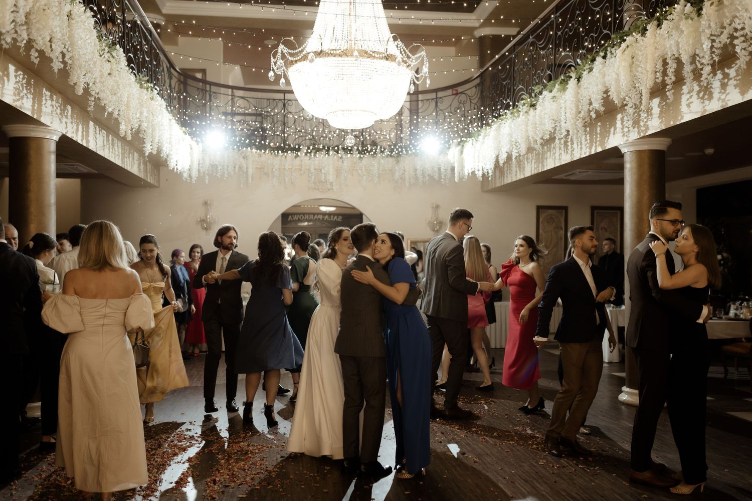 Couples dance beneath an elegant crystal chandelier during an elegant wedding reception in a vintage ballroom.