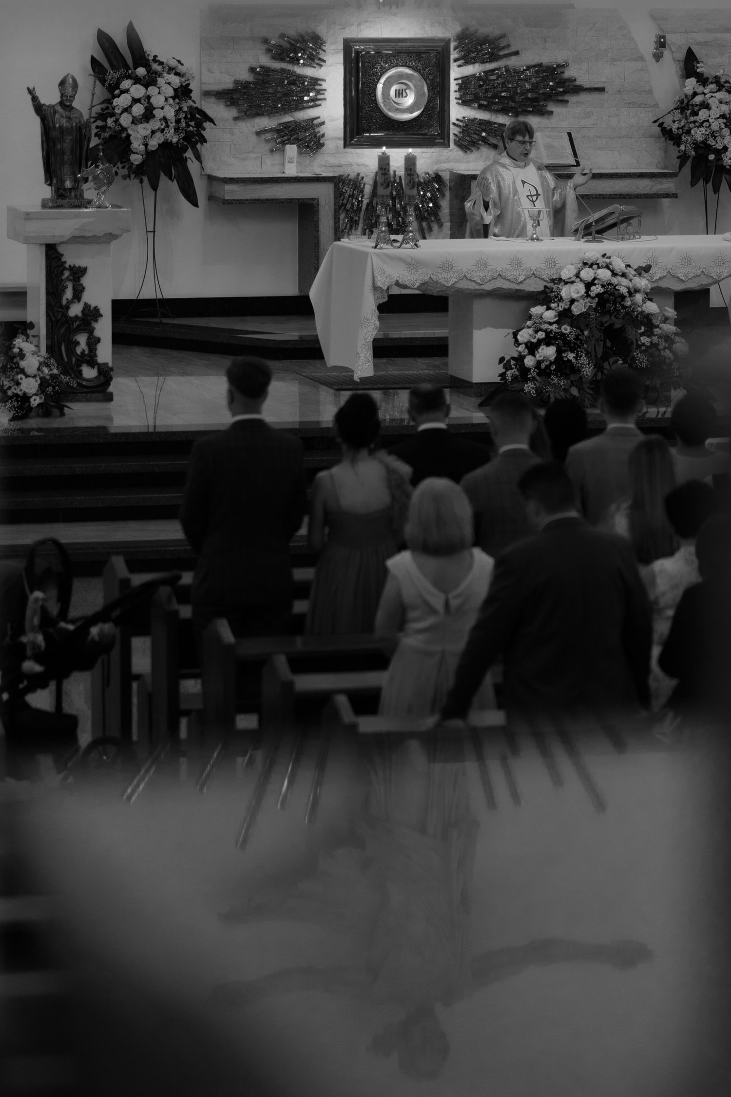 Black and white photo of a church interior during a service with floral arrangements decorating the altar area.