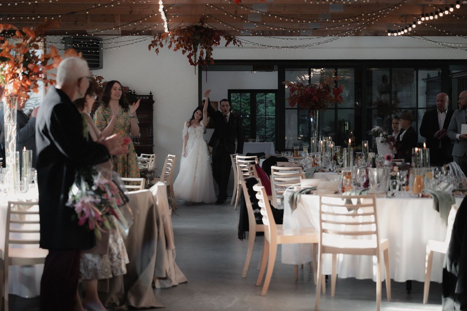 An elegant wedding reception venue with white tables, chairs and string lights decorating the rustic industrial ceiling.