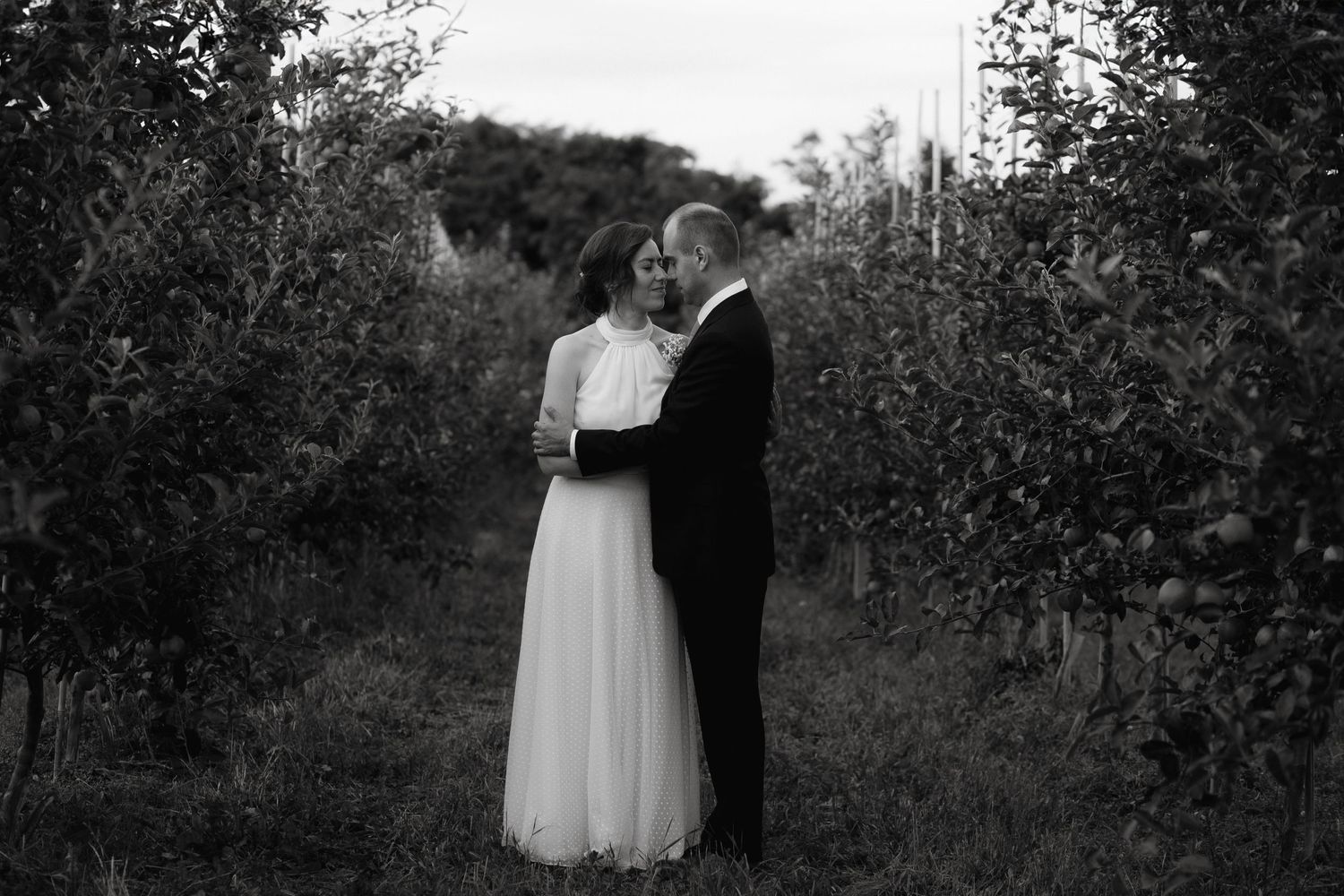 Black and white romantic wedding portrait of couple embracing outdoors in a garden setting at dusk.