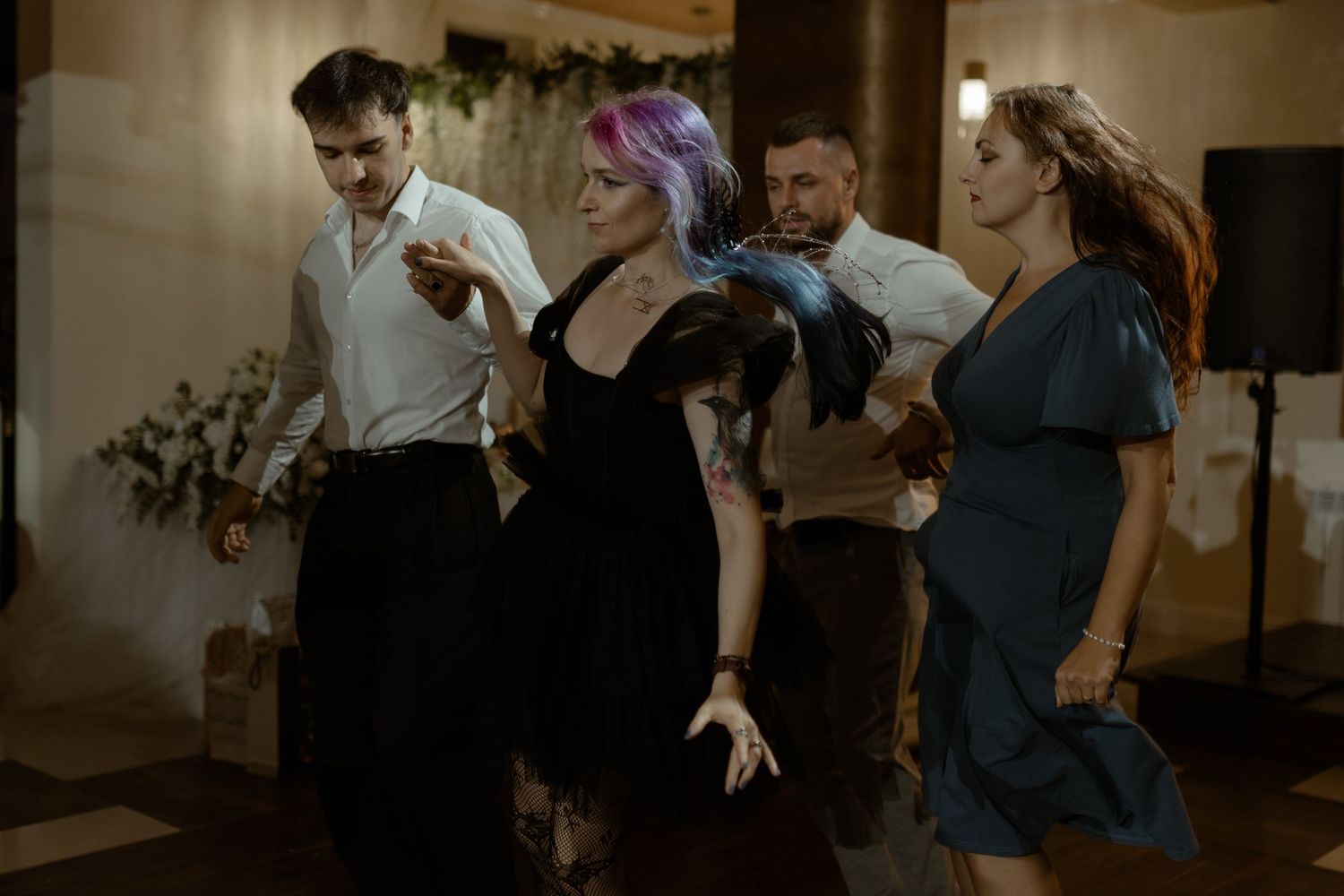 People dancing energetically at a social event with decorative lights in the background.