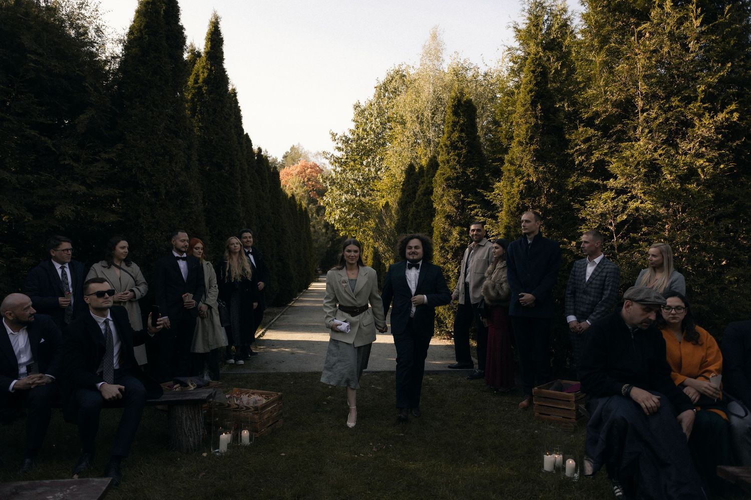 Wedding guests gather along a tree-lined garden path during an outdoor autumn ceremony.