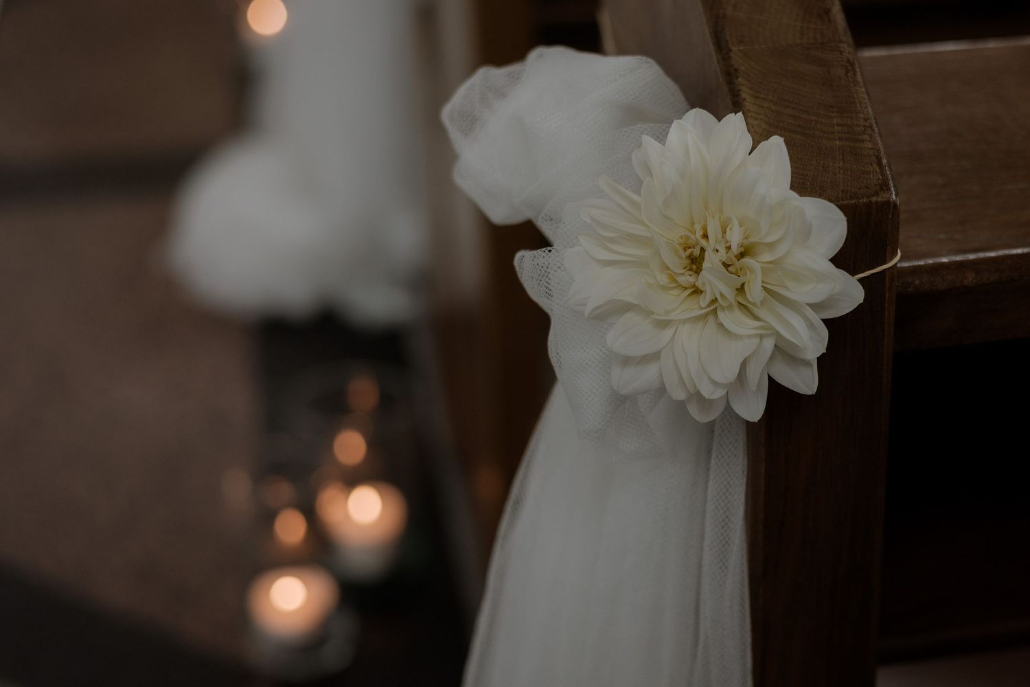 A white dahlia flower decorating a pew with soft candlelight bokeh in the background.