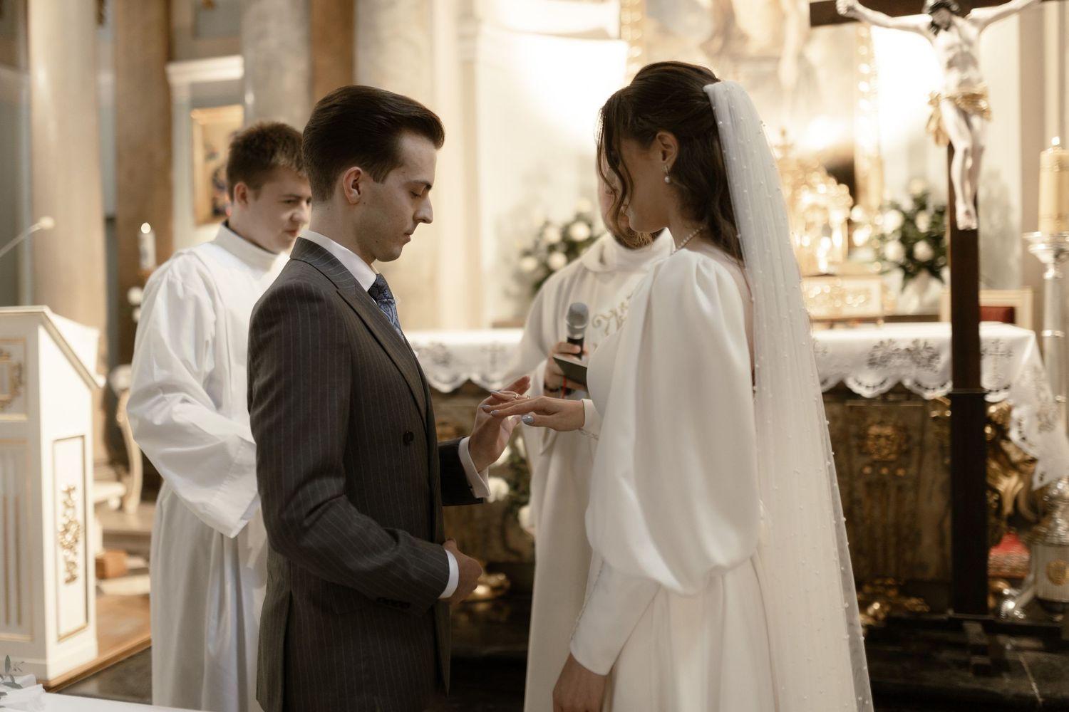 A ceremony takes place in an elegant indoor setting with white decor and floral arrangements.