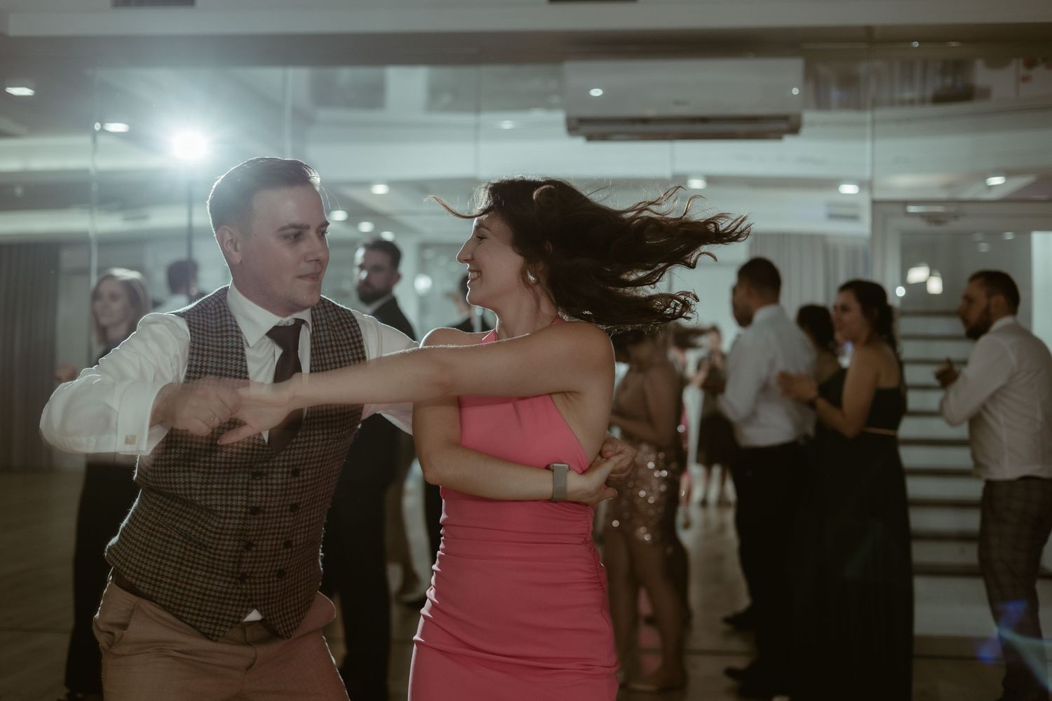 Two dancers in formal attire perform at a reception venue as her pink dress flows with the movement.