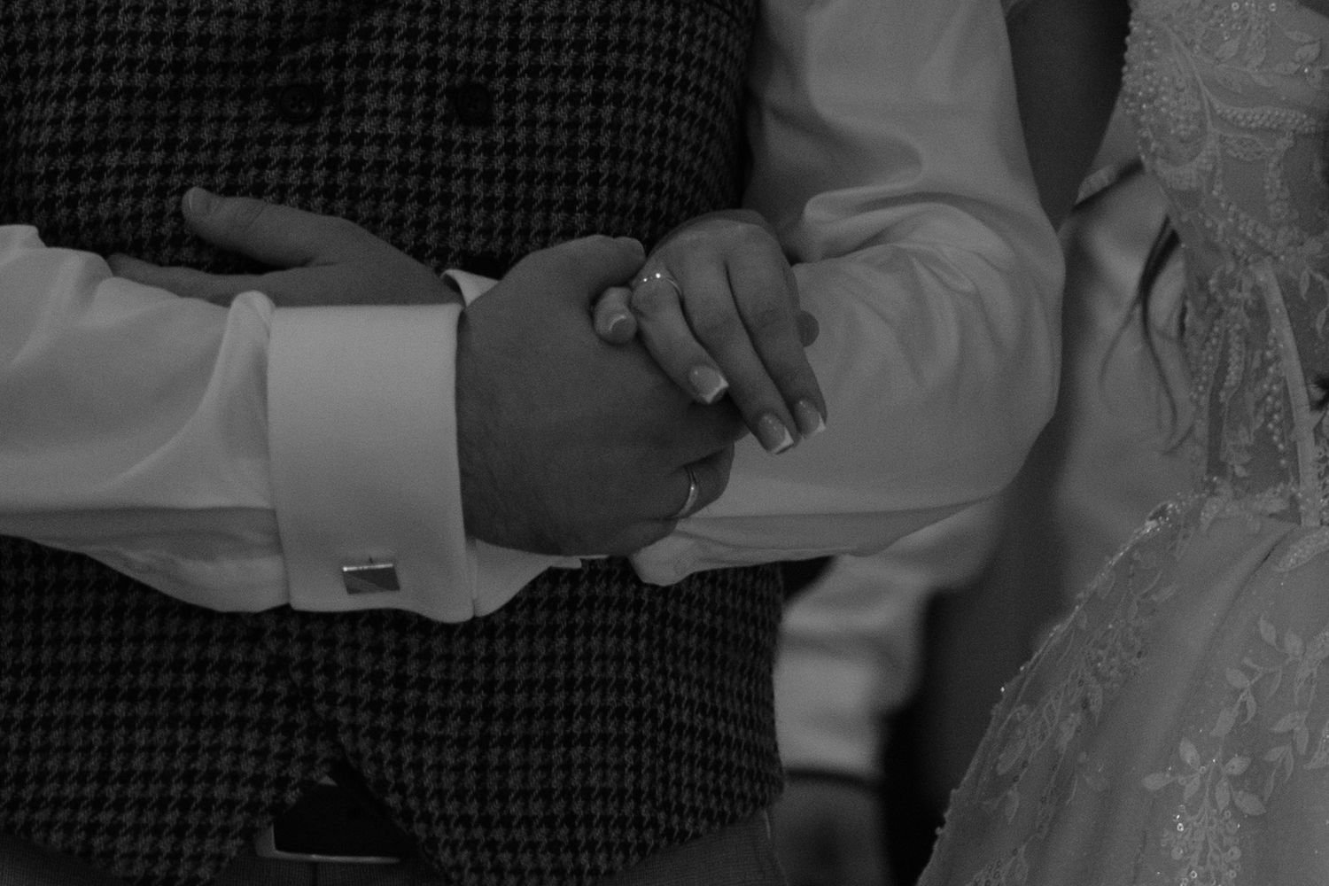 A black and white close-up of hands clasped together, with one wearing formal attire including a cuff link.