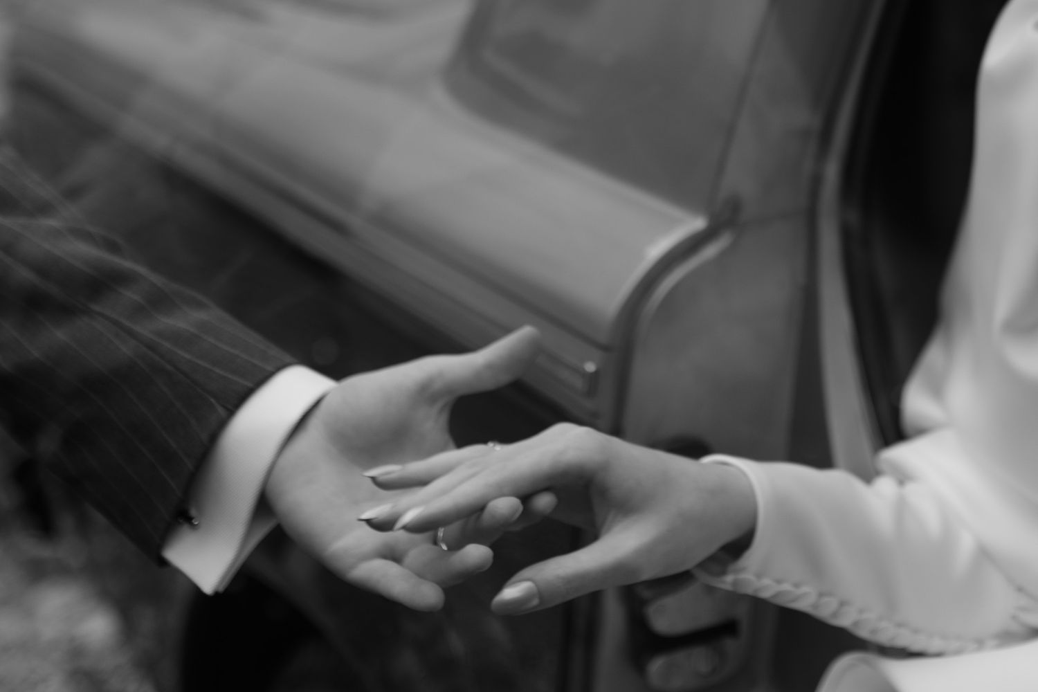 A black and white close-up photograph of two hands reaching towards each other in a tender moment.