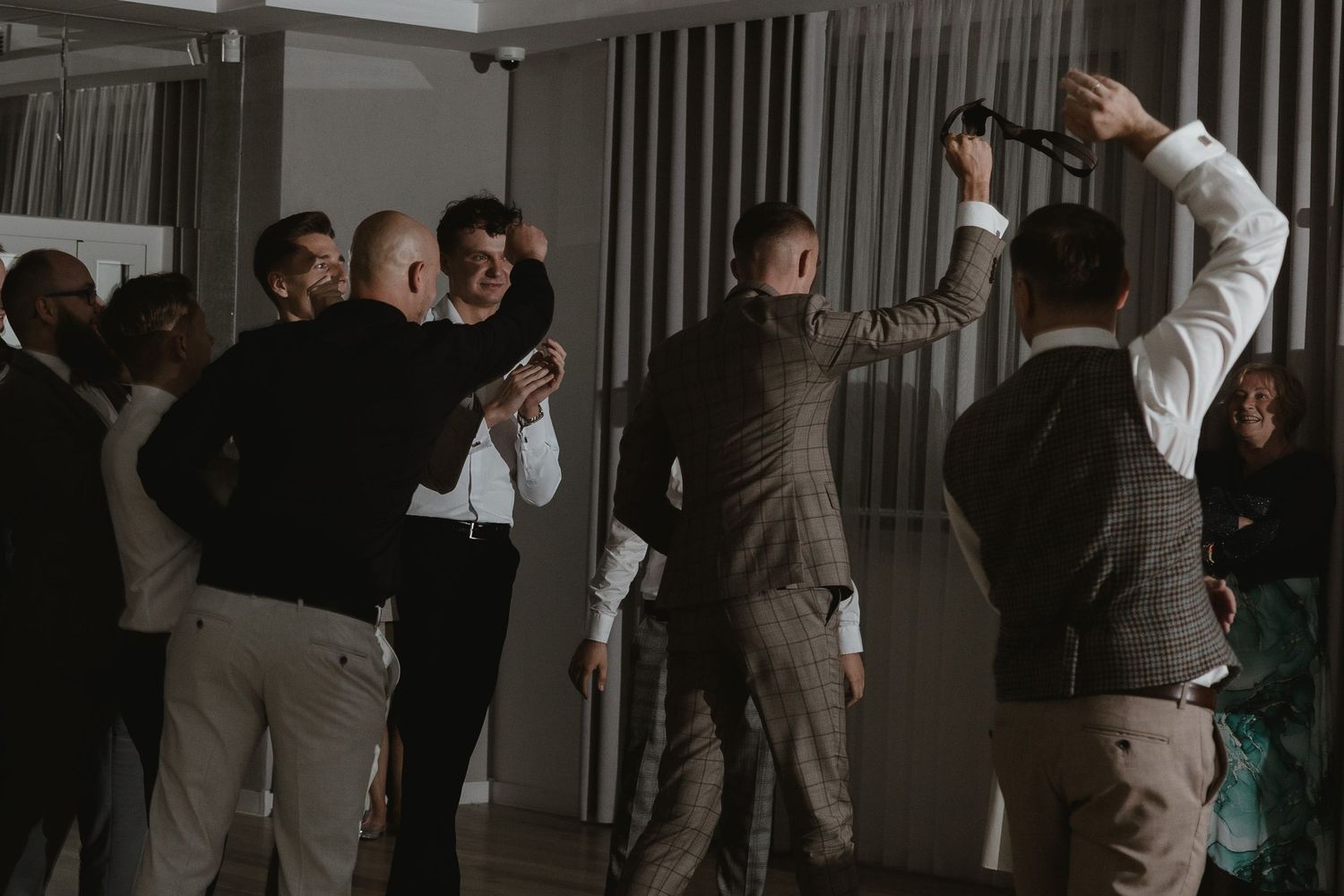 Group of people in formal attire congregate together in a dimly lit room along a wall.