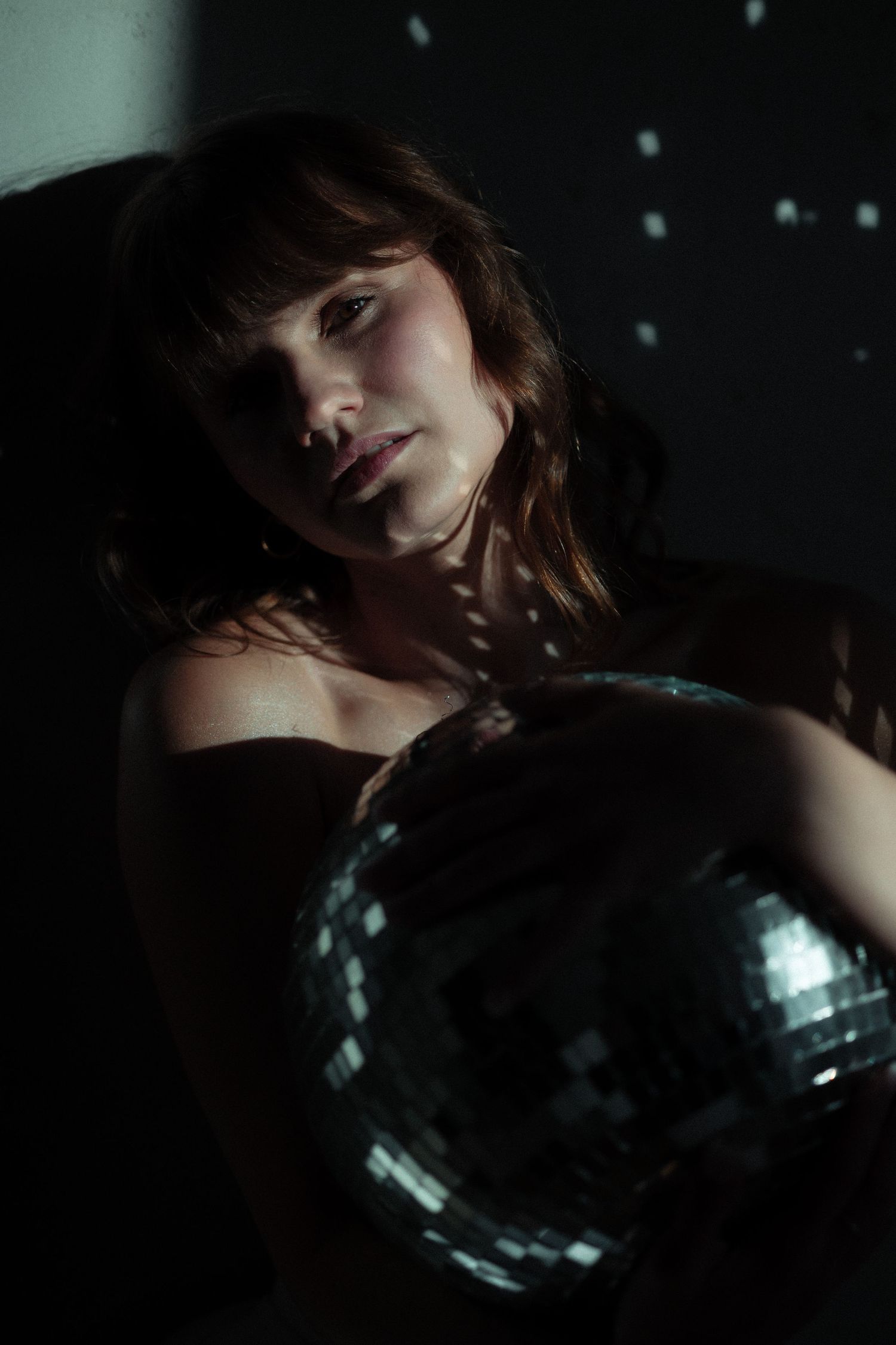 Dramatic close-up portrait with disco ball reflections in dark ambiance.
