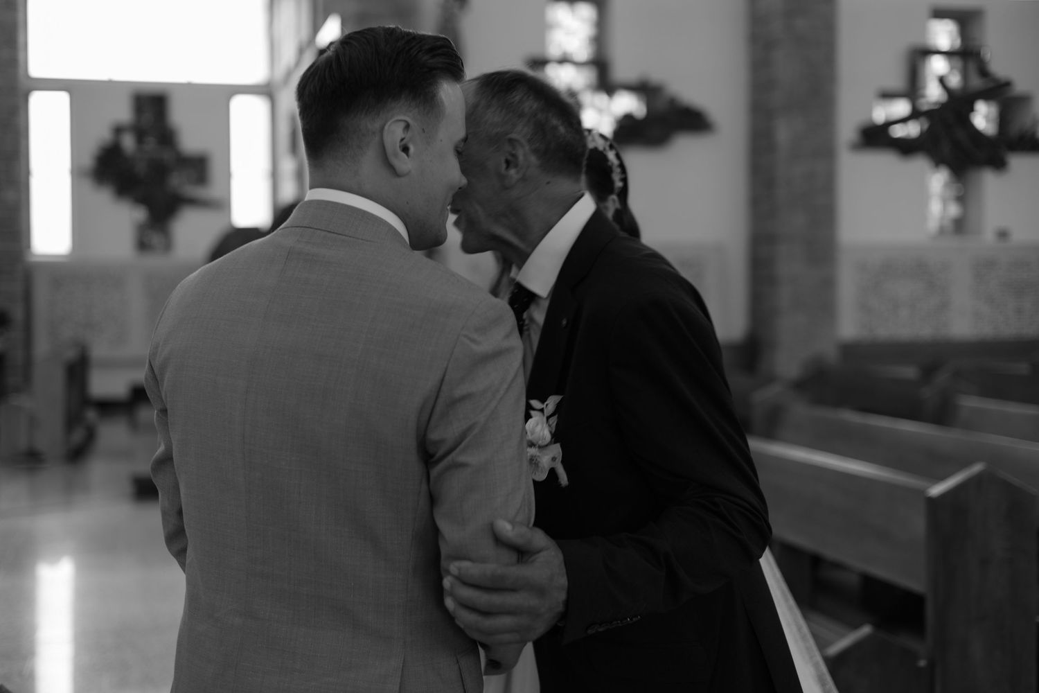 A black and white photograph shows two people having an intimate moment in what appears to be a church setting.