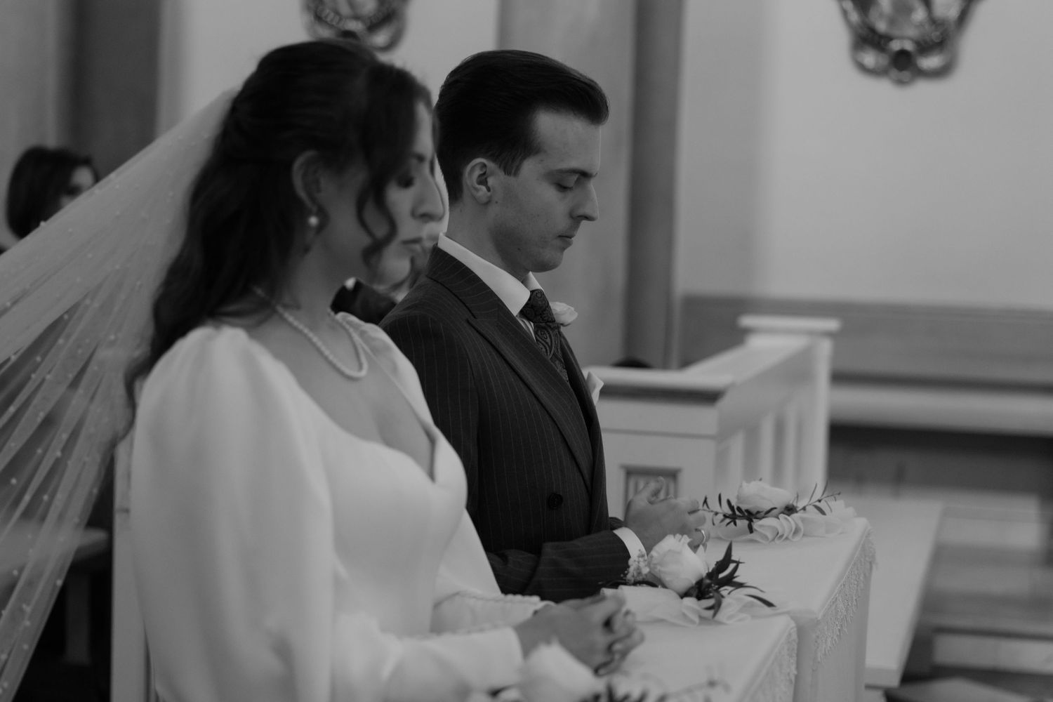 A couple in formal wedding attire stands together during a black and white church ceremony.