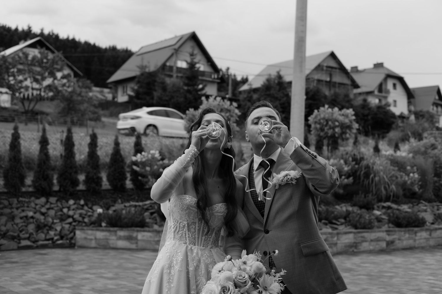 A happy couple poses outdoors making silly faces at their wedding with houses in the background.