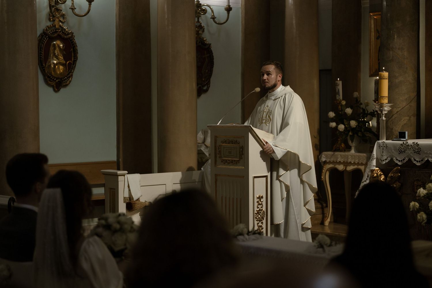 A clergy member delivers a sermon from the pulpit in a dimly lit church during a religious service.