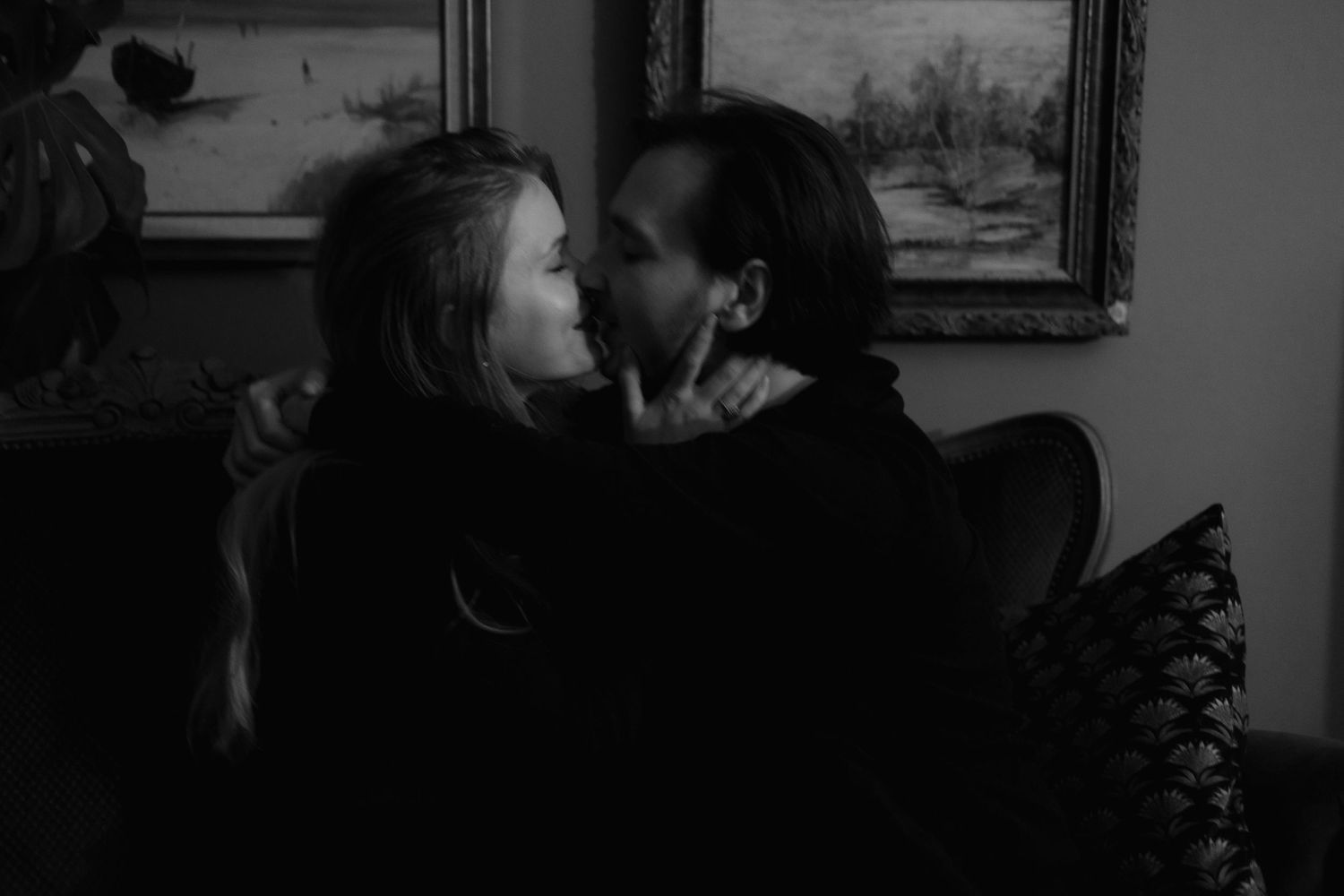 A romantic black and white photograph shows a couple in an intimate moment on a couch with framed artwork visible in background.