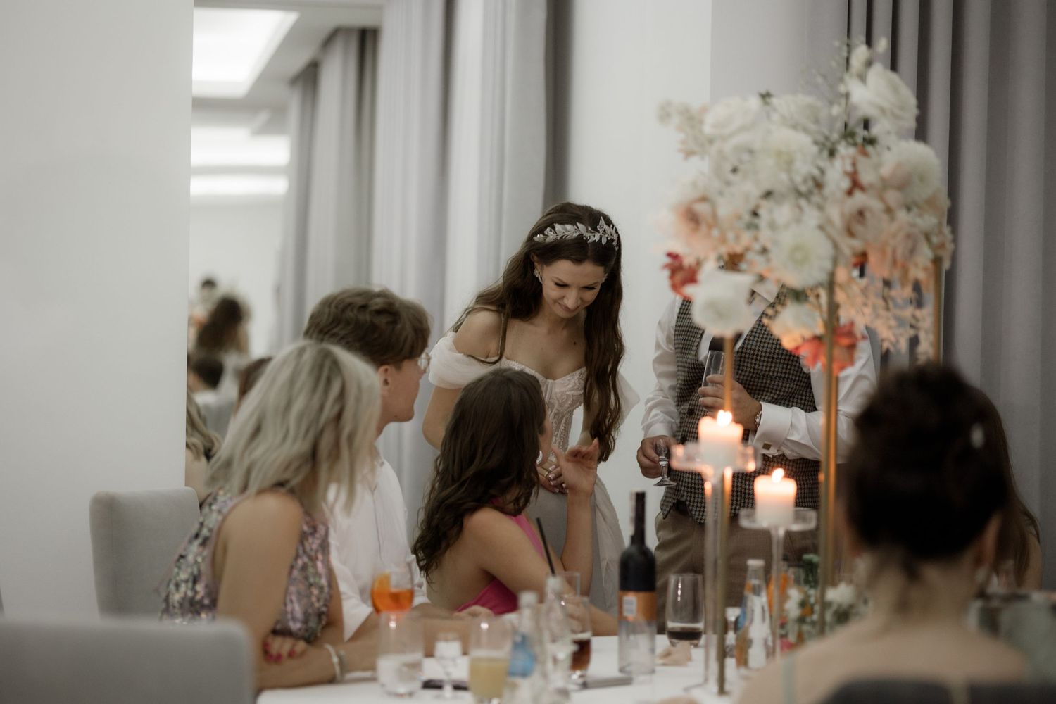 Elegant wedding reception scene with candlelit table, floral arrangements and guests gathered in conversation.