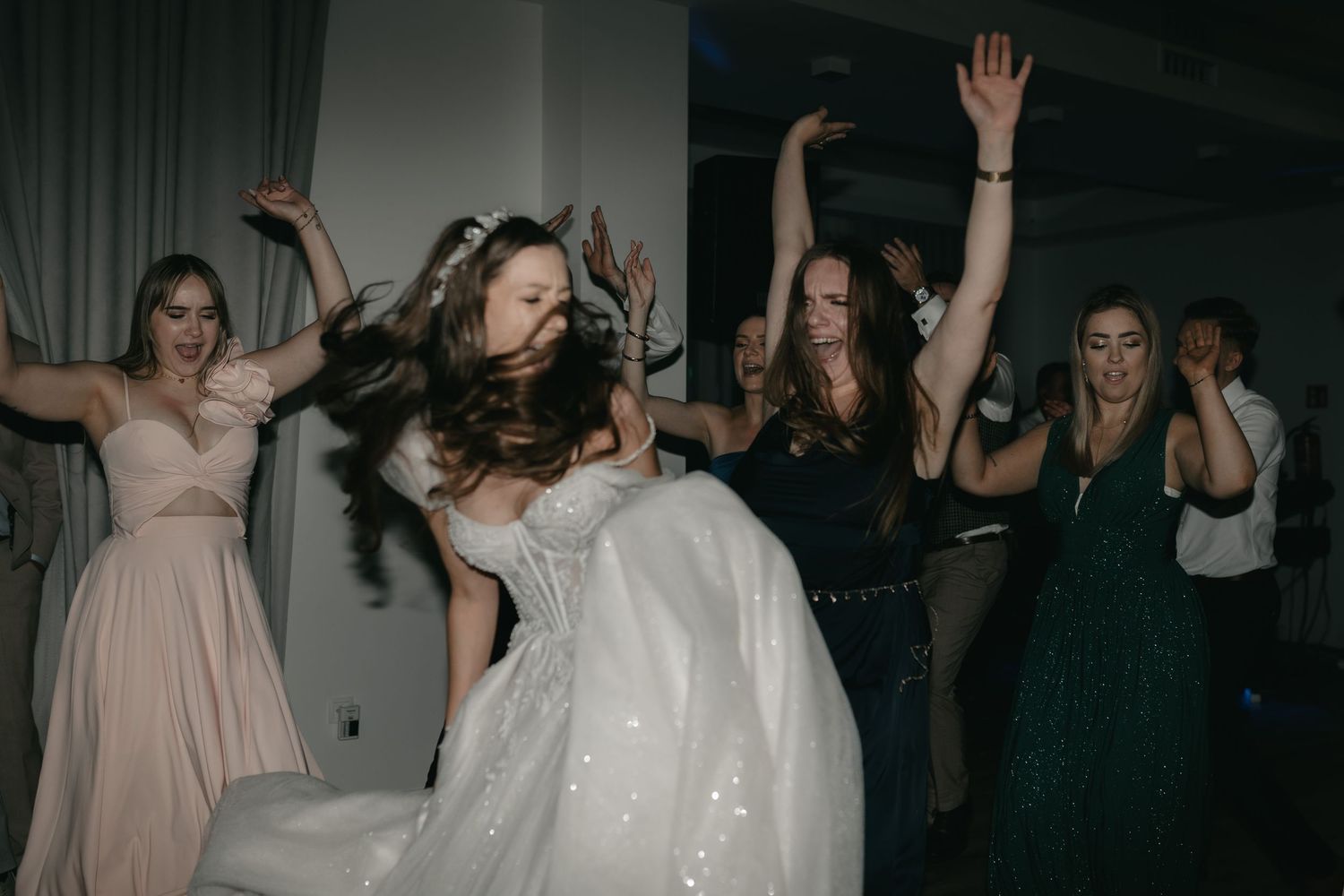People in formal attire dancing energetically at a celebration with dark atmospheric lighting.