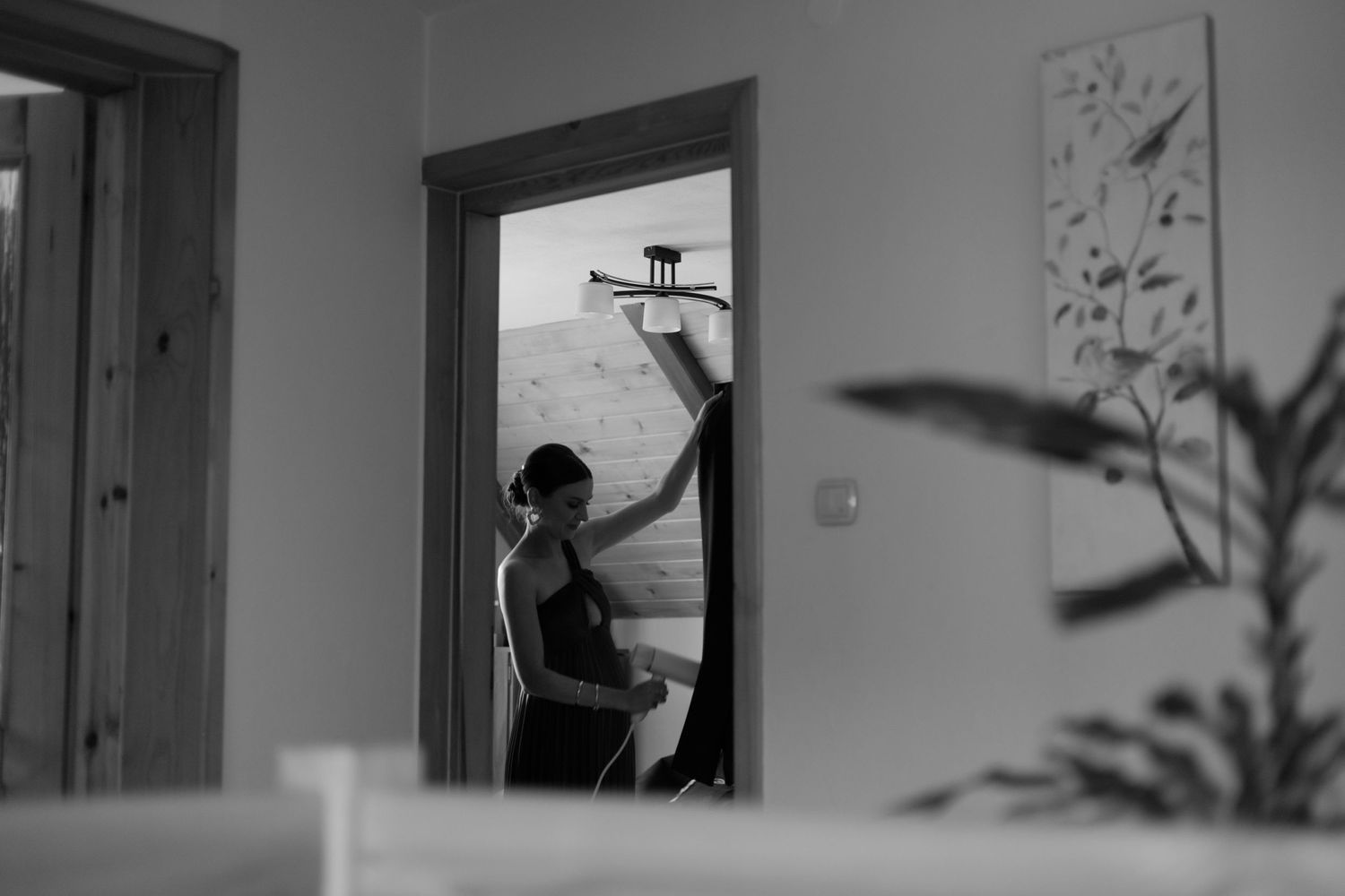 A silhouette in a doorway reaches up towards a window at home, captured in black and white photography.