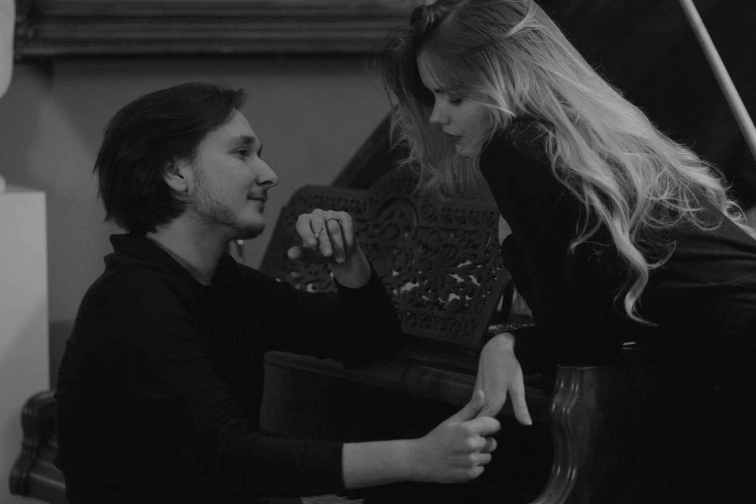 Two people in black clothing share an intimate moment in a dramatic black and white photograph.