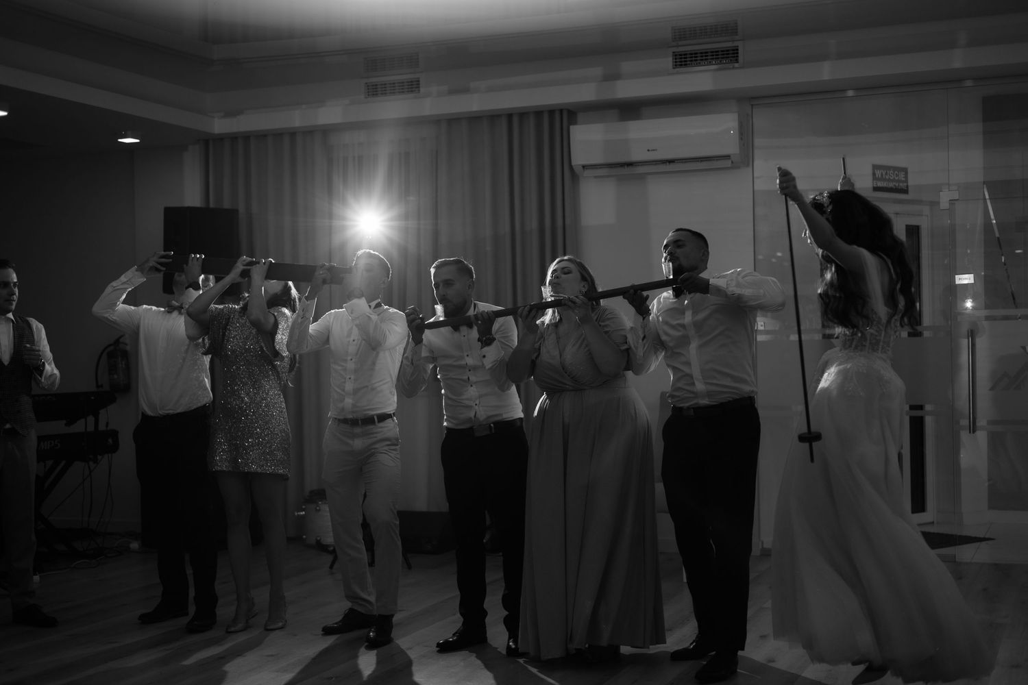 Wedding party dancing and celebrating together at an indoor reception venue in black and white.