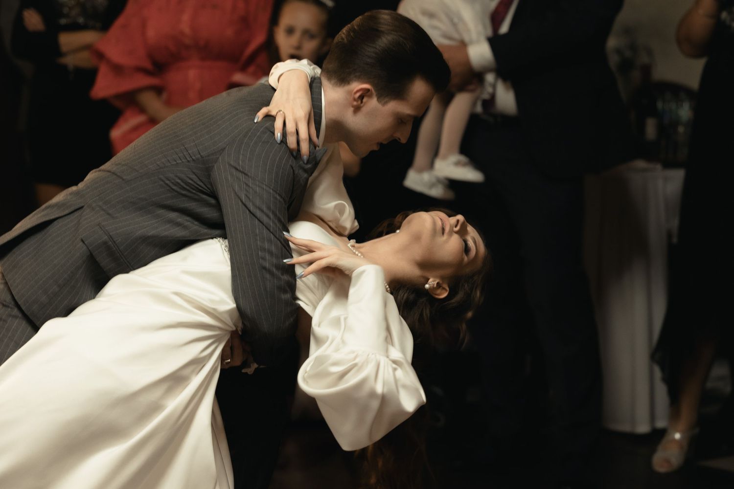 Couple performs elegant dip dance move during wedding reception on dark dance floor.