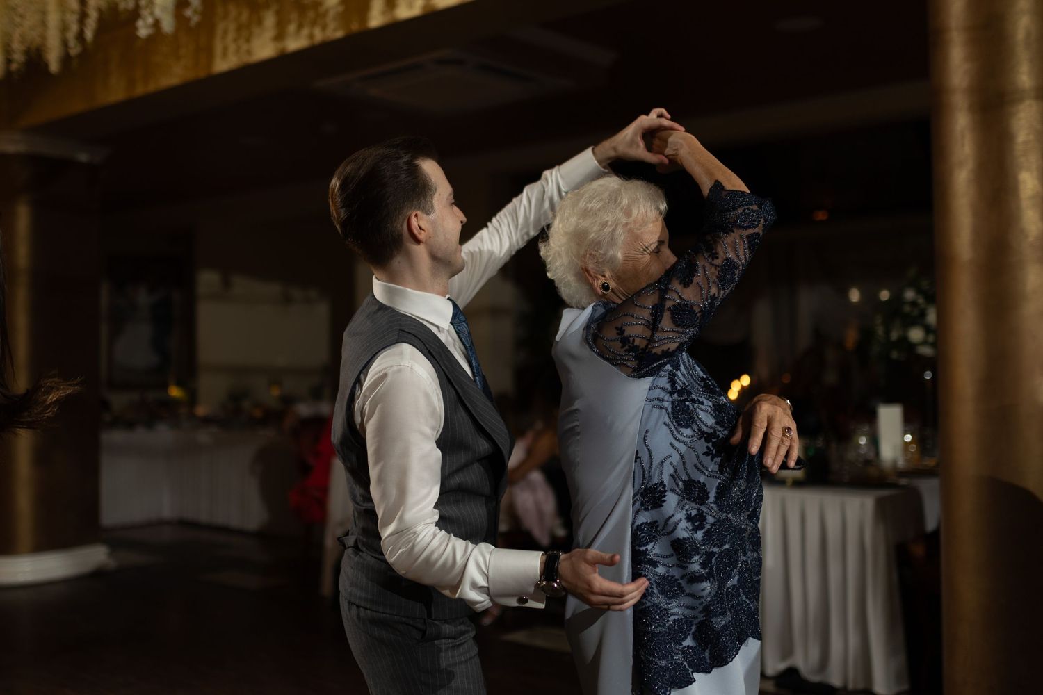 Two dancers move gracefully together during a slow dance at an indoor event venue with dim atmospheric lighting.
