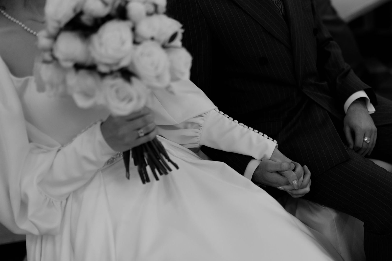 Black and white close-up of a wedding bouquet being held with white roses and formal attire visible.