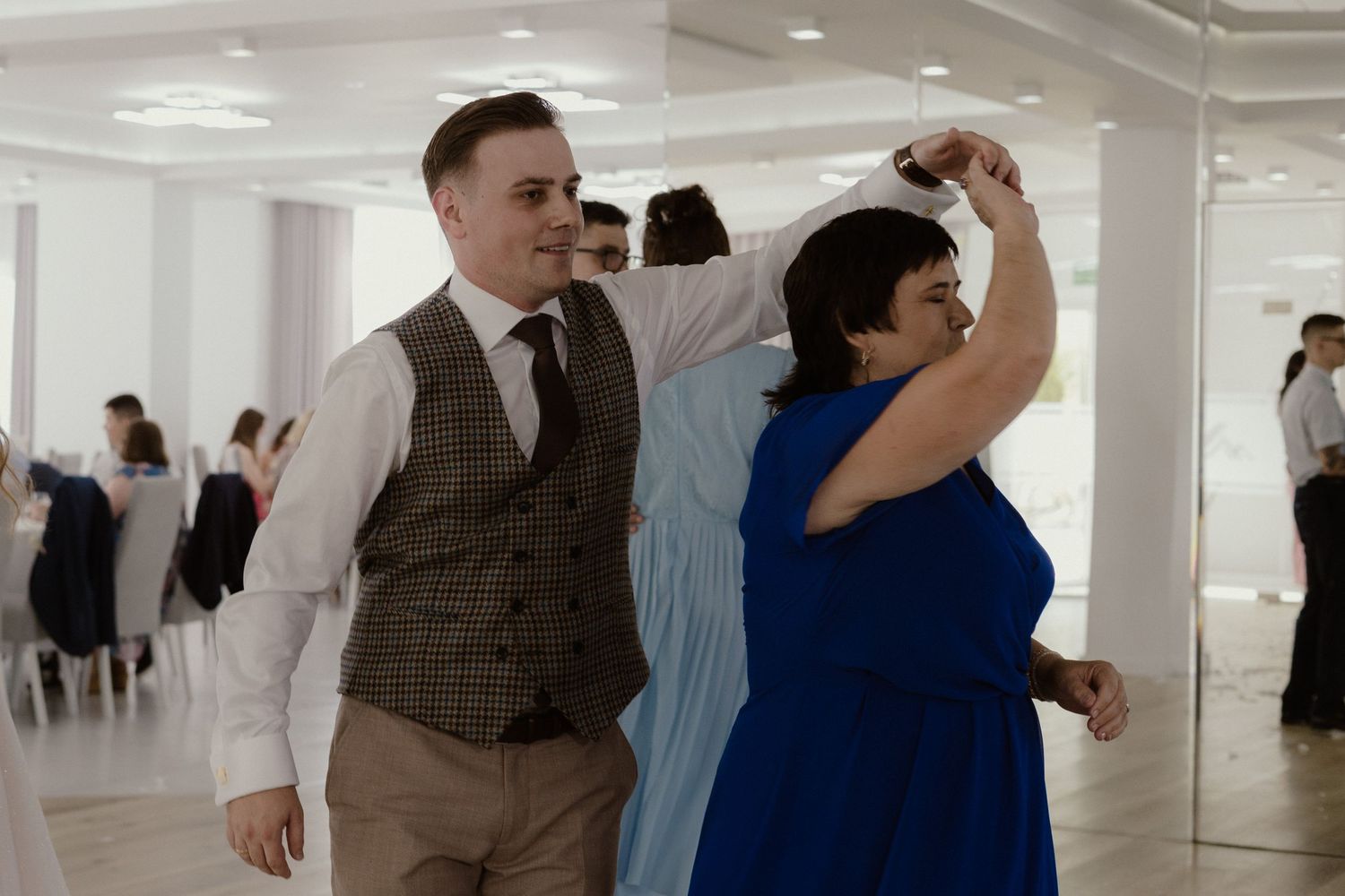 Dancing partners move gracefully together in formal attire at an elegant event venue with white decor.