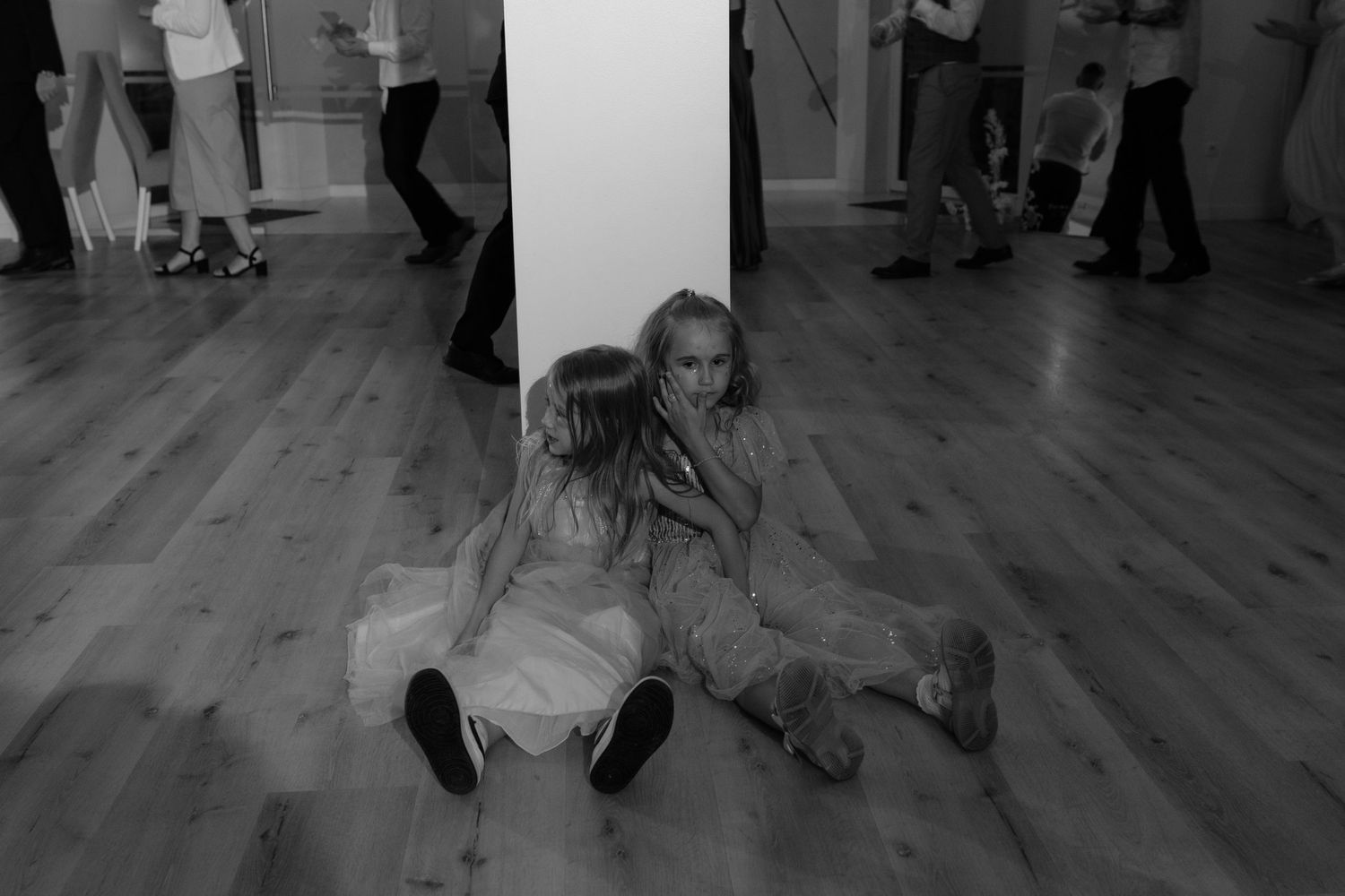 A black and white image shows a dancer in light colored clothing sitting on a dance studio floor near a mirrored wall.
