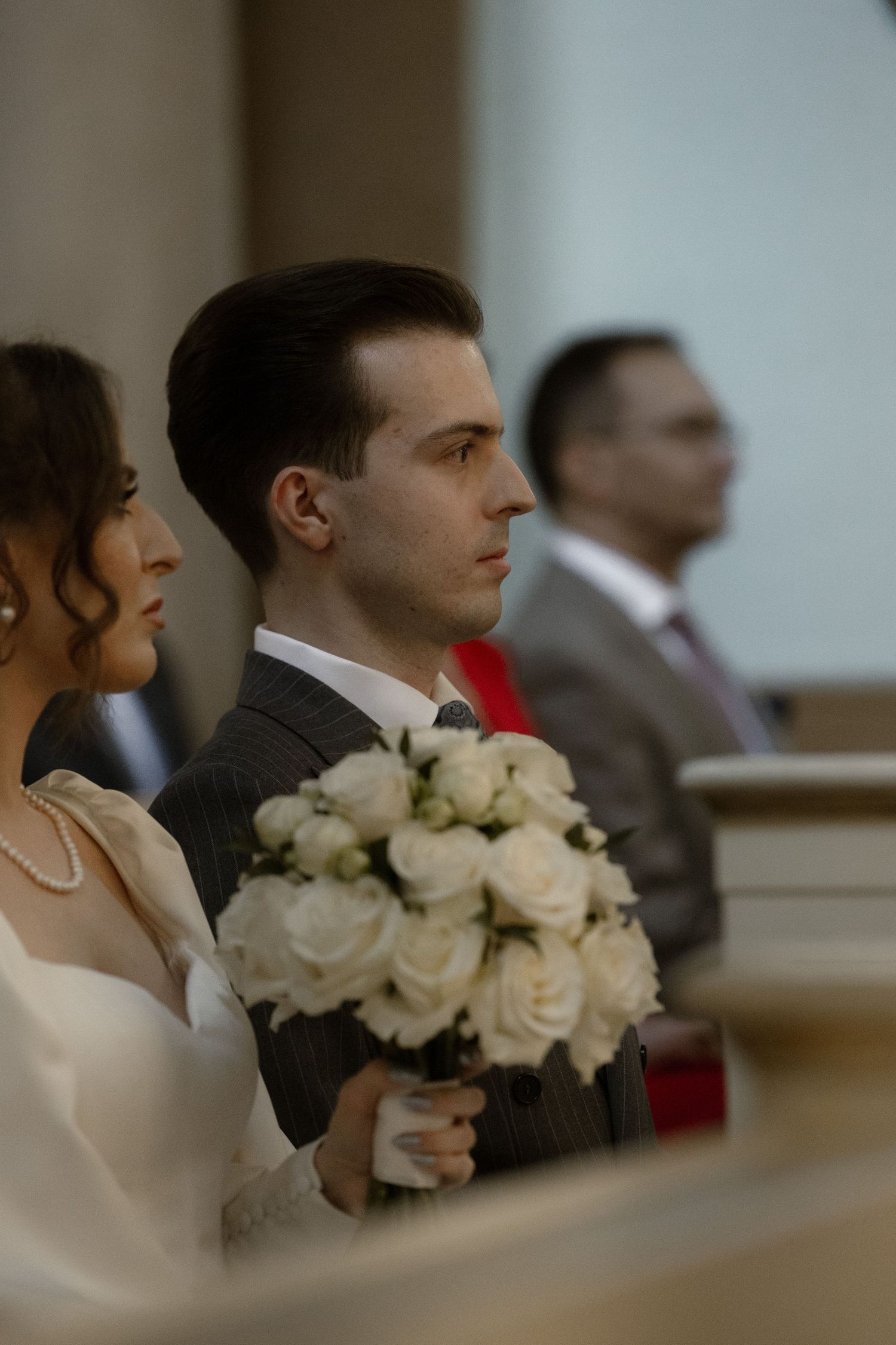 Couple at wedding ceremony with bride holding elegant white rose bouquet in church.