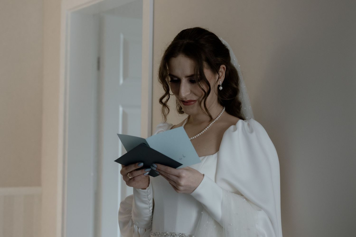 Someone in a white sweater holds and reads a small book near a window with soft natural lighting.