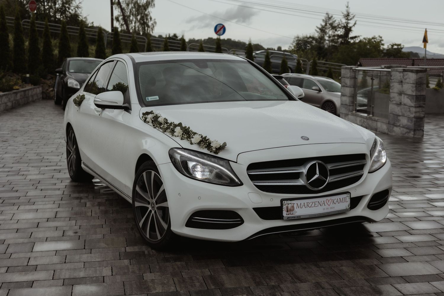 White Mercedes-Benz C-Class sedan parked on stone pavement with wedding decorations on the hood.