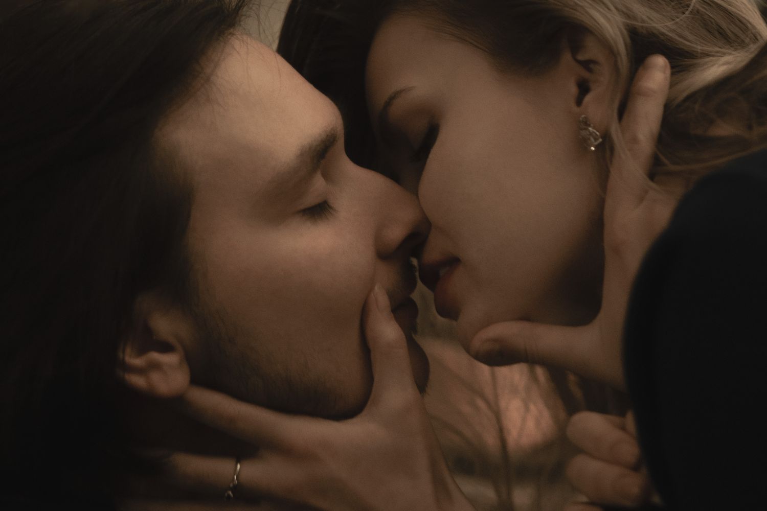 A romantic couple sharing an intimate kiss in moody, low-key lighting creating a sensual atmosphere.