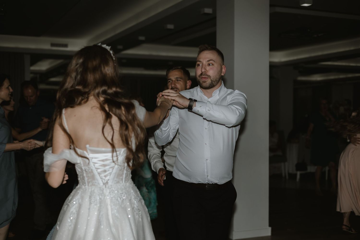 Two people dance together at a wedding reception in a dimly lit venue while the bride wears a white corset-style dress.