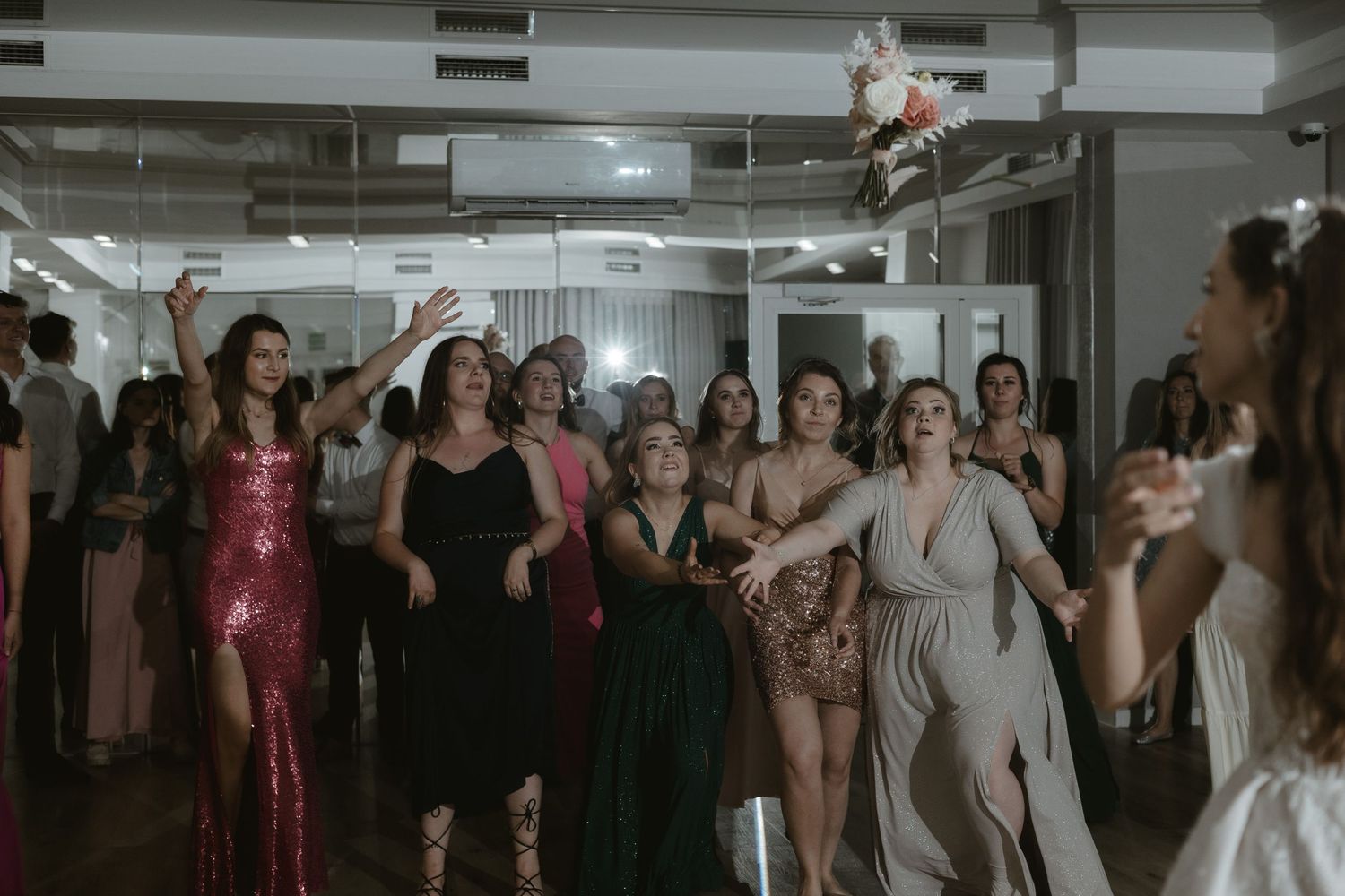 A group of party guests in formal attire dance and celebrate together in an industrial-style venue.