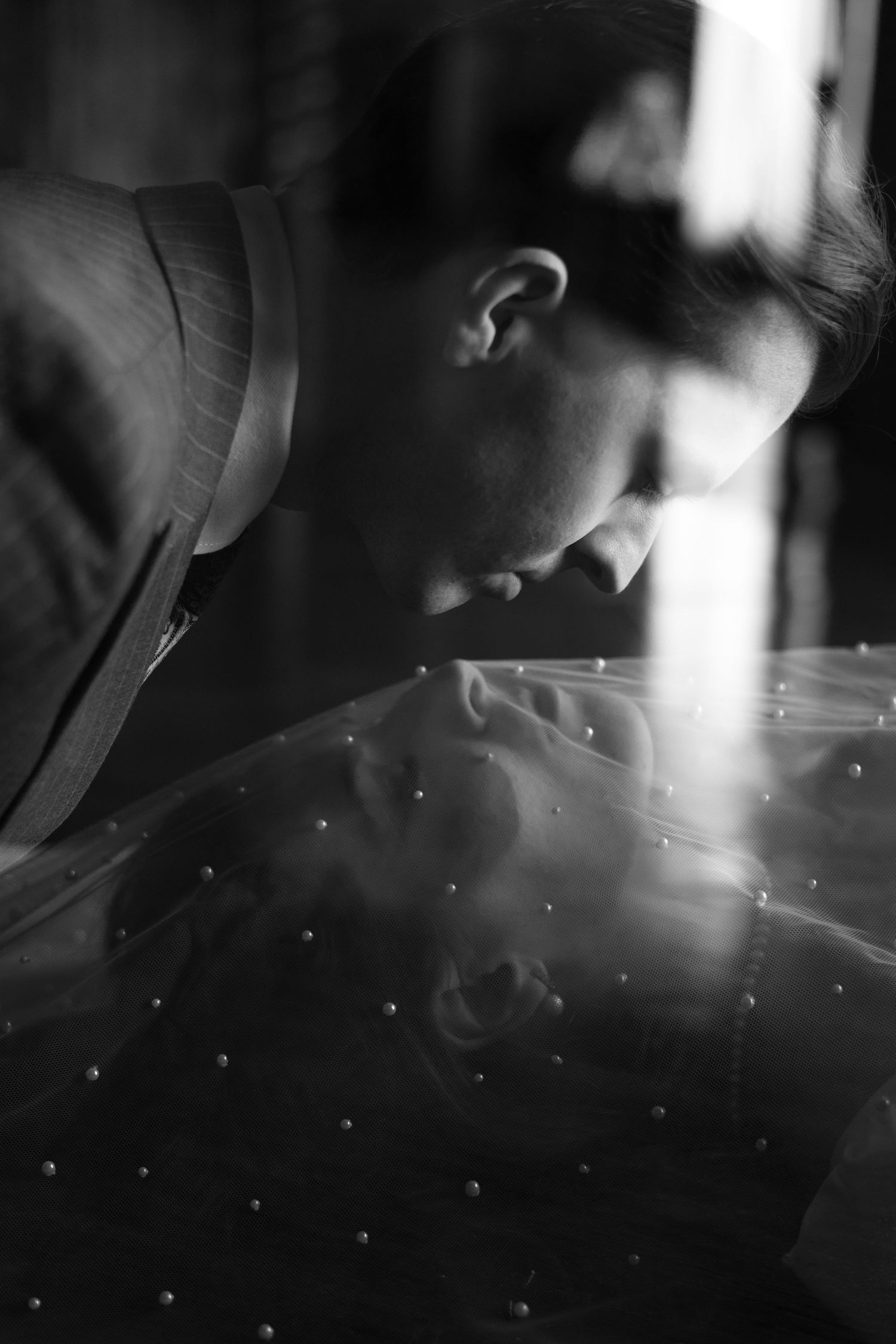 Artistic black and white photograph of person in profile looking down with dramatic shadows and light beams.