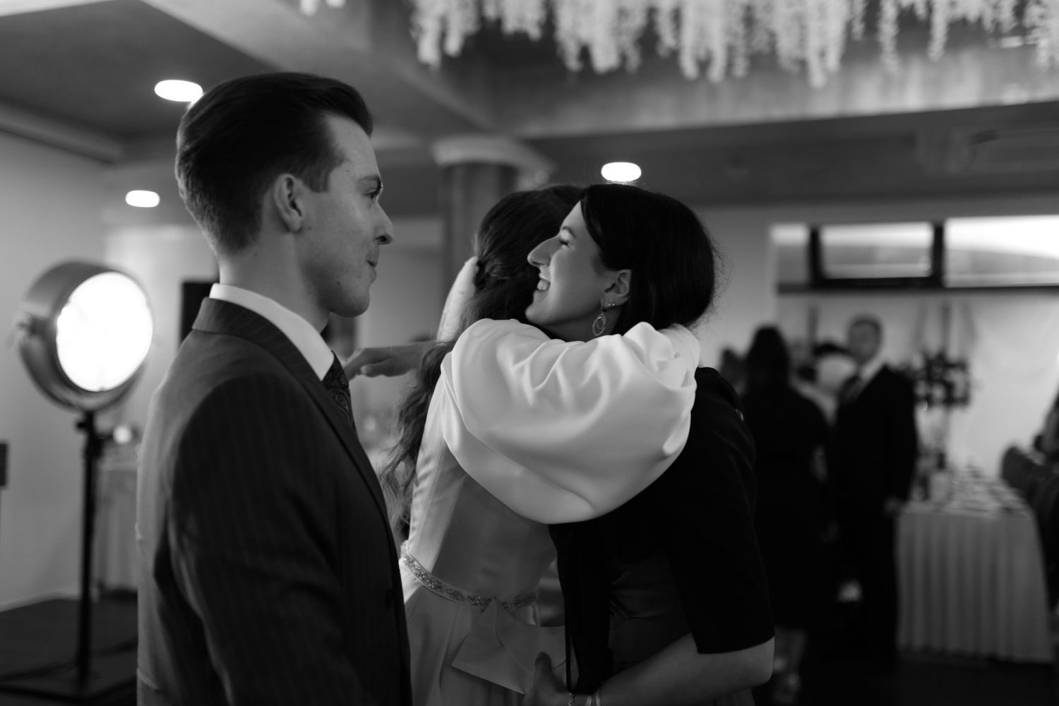 A black and white photograph showing a couple dancing together at an elegant event with chandeliers visible above.